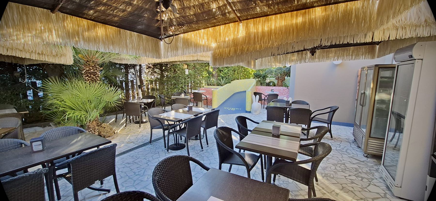 Il giardino del 490 con i tavoli sotto gli ombrelloni di paglia, tra le palme